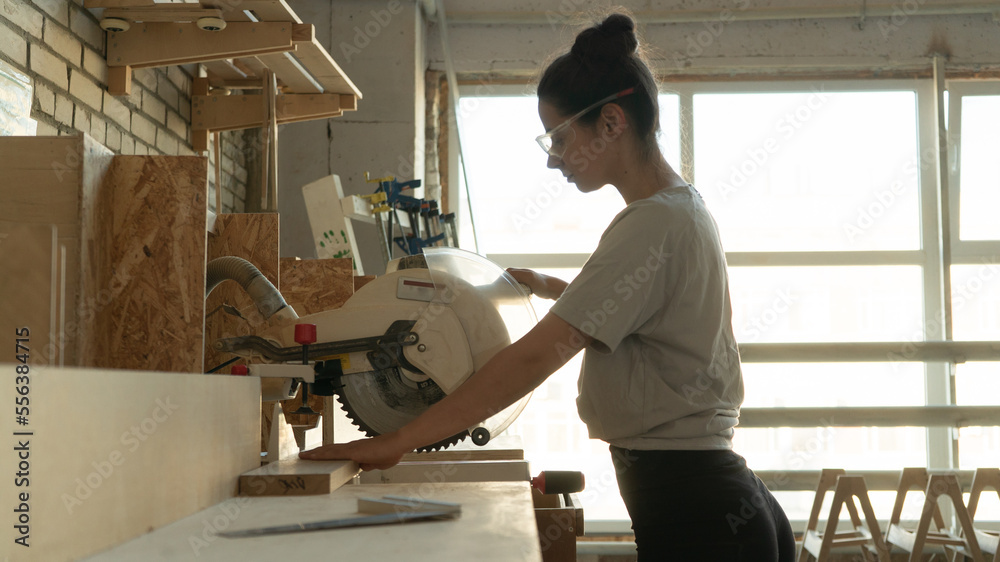 girl carpenter cuts a board on a miter saw