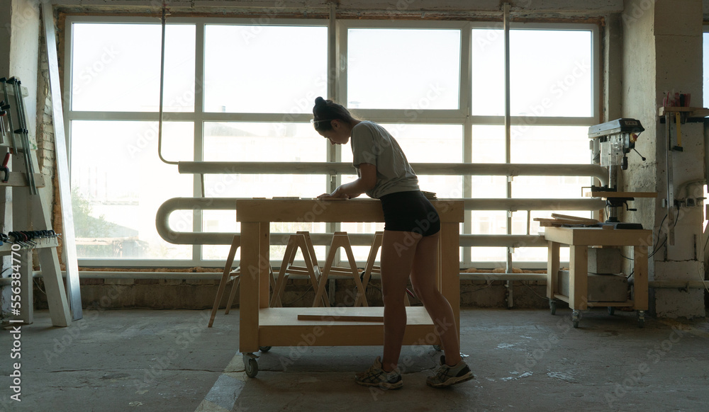 a carpenter girl stands at a workbench at a workbench and grinds a wood blank