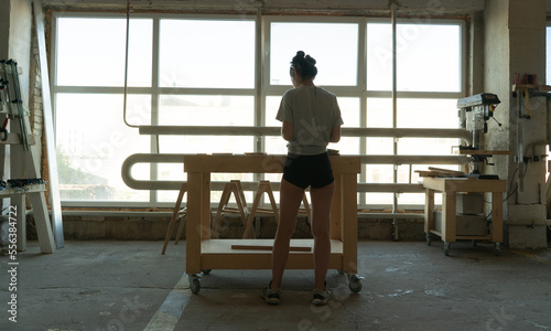 girl carpenter stands behind a workbench and works with a wooden blank
