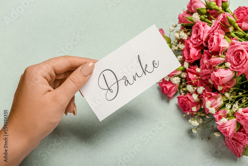 Female hand with card and beautiful bouquet on color background, closeup
