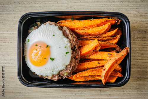 Healthy bison breakfast meal with ground bison patty arranged on a bed of sweet potatoes, celery, and green onion topped with an egg prepared in a to-go container