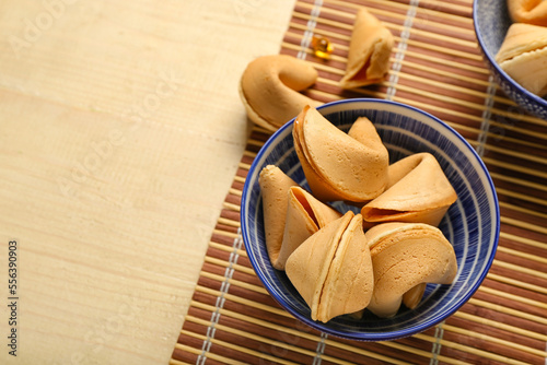 Bamboo mat with bowl of fortune cookies on wooden background, closeup