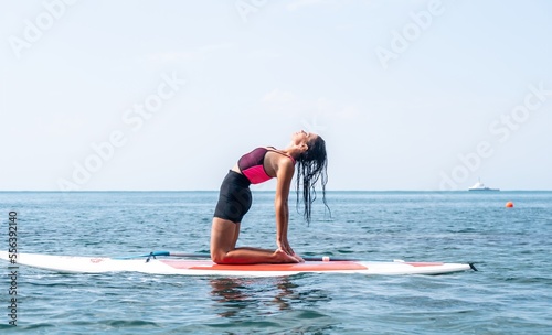 Woman sup yoga. Happy young sporty woman practising yoga pilates on paddle sup surfboard. Female stretching doing workout on sea water. Modern individual female outdoor summer sport activity.