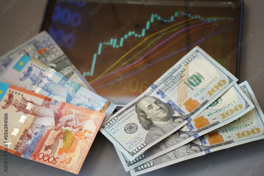 Almaty, Kazakhstan - 10.04.2022 : Stock charts on the tablet and tenge and dollar banknotes on the table. Almaty, Kazakhstan - 10.04.2022 : Stock charts on the tablet and tenge and dollar banknotes on the table.