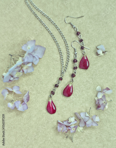 Close up craft jewellery set with red petals and fresh flowers concept photo. Top view photography with plywood on background. High quality picture for wallpaper, travel blog, magazine, article