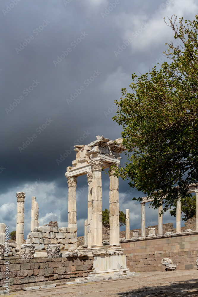 Obraz premium The ruined Temple of Trajan in Pergamon Ancient City. Corinthian order stone-cut relief on the frieze. Dramatic sky at background. History, art or architecture concept. Bergama, Turkey
