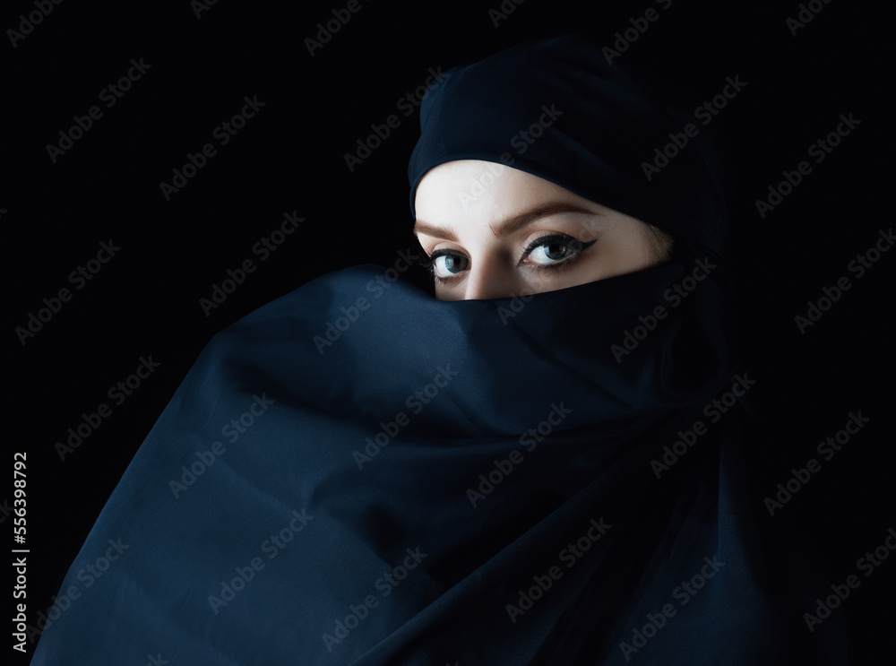 Portrait of young woman wearing hood on black background.