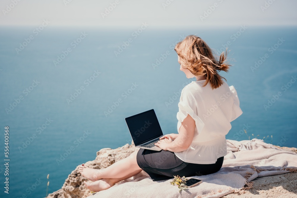 Woman sea laptop. Successful business woman working on laptop by the sea. Pretty lady typing on computer at summer day outdoors. Freelance, digital nomad, travel and holidays concept.