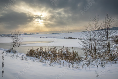 Winter snowy landscape with frozen pond and sun rays