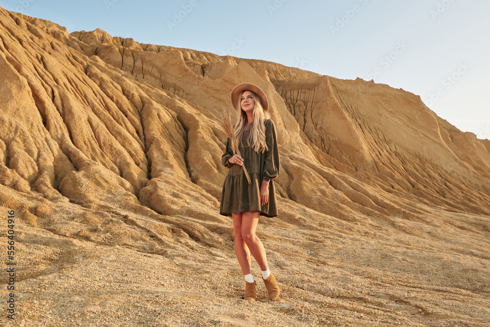 young beautiful woman with long beautiful blond hair in a hat and with grass in her hands against the backdrop of a beautiful sandy desert landscape