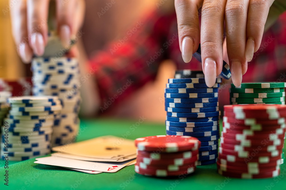 Female hand with playing cards and poker chips close-up in front of poker table. Female hand with playing cards and poker chips close-up in front of poker table.