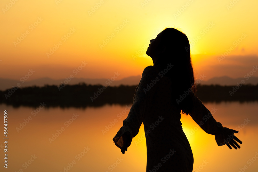 GOLDEN LIGHT SILHOUETTE: Calm beautiful smiling young asian woman in white dress breathing fresh air outdoor on peaceful evening. relaxing with eyes closed, feeling alive, breathing, dreaming.