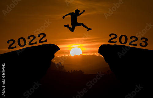 A young man jump between 2022 and 2023 years over the sun and through on the gap of hill silhouette evening colorful sky. happy new year 2023. © kanpisut
