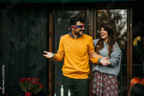 A blindfolded man navigated by his wife is about to be surprised by a group of friends during a garden party.