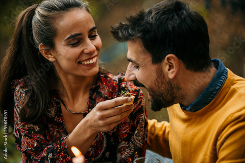 Group of people sitting around a table in garden restaurant and having meal together. Woman is feeding a man