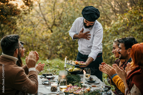 Group of diverse people enjoying summer afternoon and evening in garden party while Chef in a white unifor went out and greeting them.