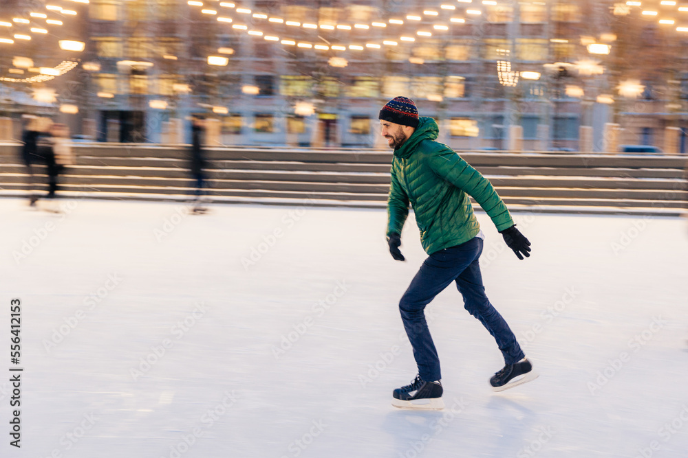 Obraz premium Middle aged male wears figure skates, being at ice rink in winter park, has fun with friend. Athlete speed skater demonstrates his talents on skating ring. Winter sport. Christmas vacations.