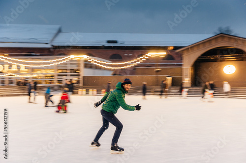 Cheerful bearded man spends Christmas time on majestic ice rink decorated with lights, skates on ice, has fun, enjoys his hobby and snowy winter weather. People, leisure, active lifestyle concept