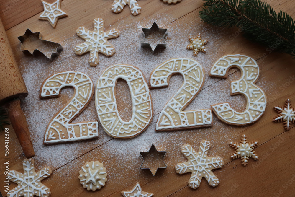 Gingerbread cookies with sugar glaze decoration in the form of numbers 2023 on wooden background. Many Gingerbread cookies in star and snowflake shape, cookie cutters and rolling pin. New year concept Gingerbread cookies with sugar glaze decoration in the form of numbers 2023 on wooden background. Many Gingerbread cookies in star and snowflake shape, cookie cutters and rolling pin. New year concept