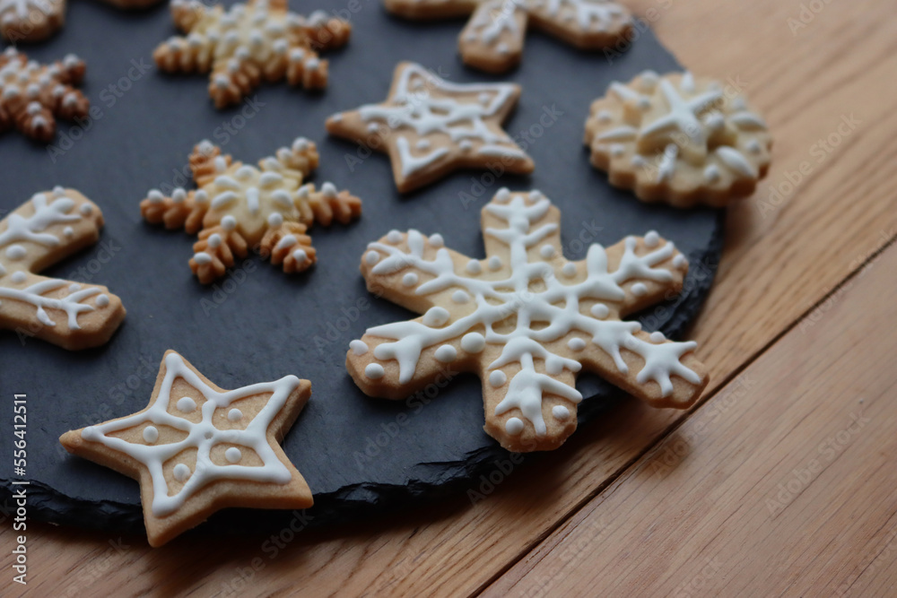 Festive gingerbread cookies in shape of Stars and Snowflakes on a black slate stone plate on wooden table Festive gingerbread cookies in shape of Stars and Snowflakes on a black slate stone plate on wooden table
