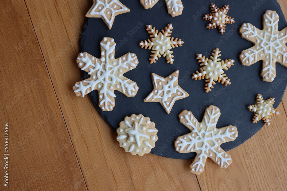 Festive gingerbread cookies in shape of Stars and Snowflakes on a black slate stone plate on wooden table