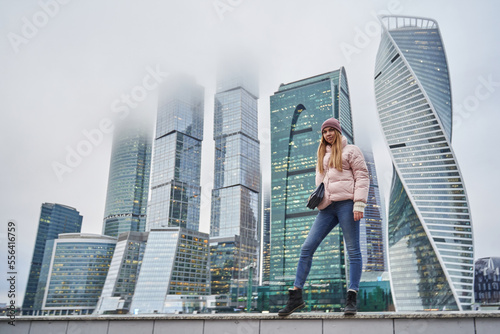 beautiful young woman next to skyscrapers and skyscrapers of a big city. tall business centers in the clouds in the background