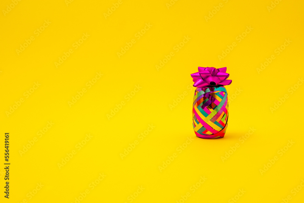 Pineapple made of colorful ribbon for gift wrapping and bow for Christmas, New year, birthday or anniversary on a yellow background. Minimal creative concept for a trendy party.