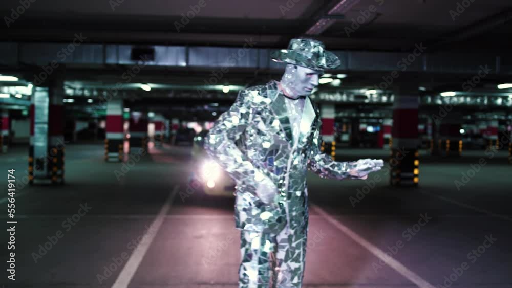 Young dancer in a mirror suit and white mask dances in the underground car park 4K