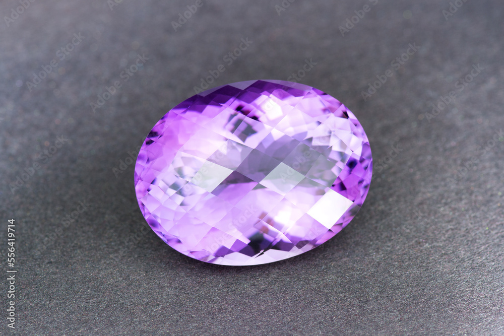 Natural Uruguay amethyst gemstone. Oval checker faceted, big size violet or purple color loose crystal clear stone setting for making jewelry. Gray textured paper background. Gemology, mineralogy. Natural Uruguay amethyst gemstone. Oval checker faceted, big size violet or purple color loose crystal clear stone setting for making jewelry. Gray textured paper background. Gemology, mineralogy.
