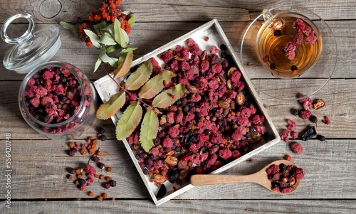 Wooden vintage background with a cup of fruit tea with dried berries of hawthorn, sea buckthorn, raspberries, plums, barberry and bird cherry.