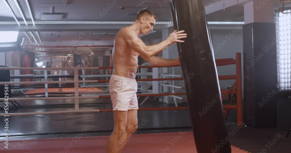 Kickboxing, athletic man fighter trains his punches, beats a punching bag, training day in the boxing gym, back lighting. Kickboxing, athletic man fighter trains his punches, beats a punching bag, training day in the boxing gym, back lighting.