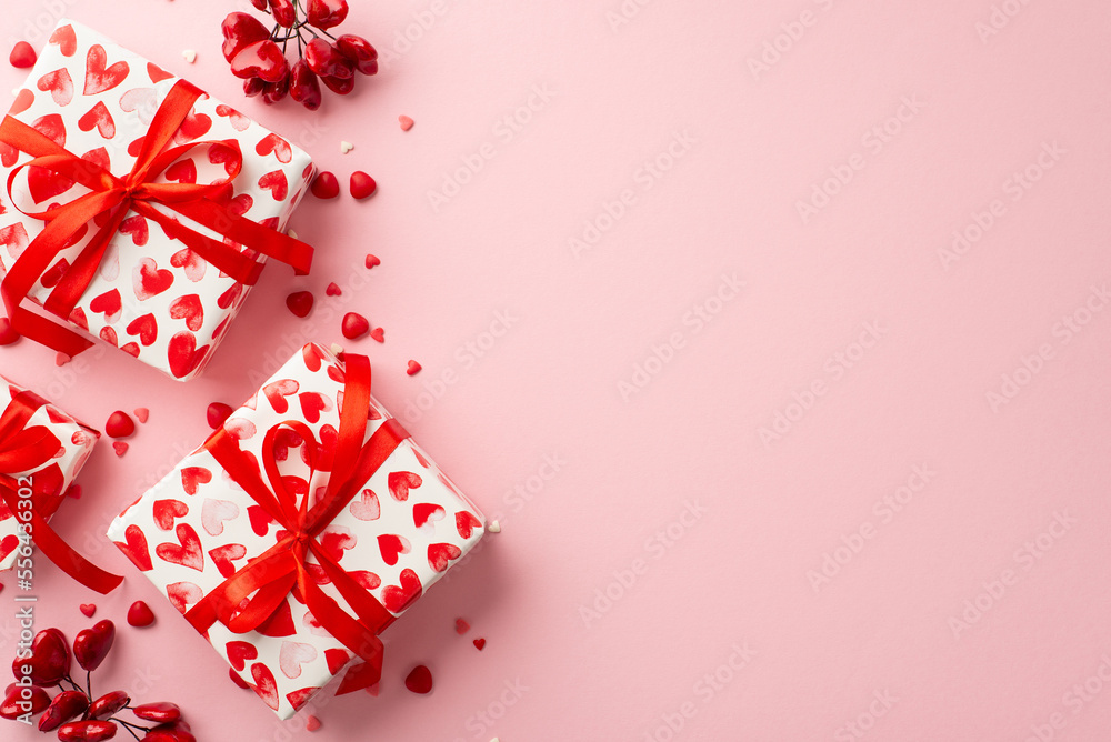Valentine's Day concept. Top view photo of present boxes in wrapping paper with heart pattern and sprinkles on isolated pastel pink background with copyspace
