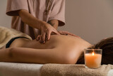 Female masseur does a relaxing back massage in a spa salon with lit candles. Concept of health, body care