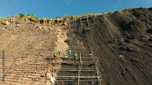 Protection of road from mountain slough, rockfall with metal accumulative restraining net fences. Workers constructing anti-landslide concrete wall prevent protect against rock slides. Rockfall photo