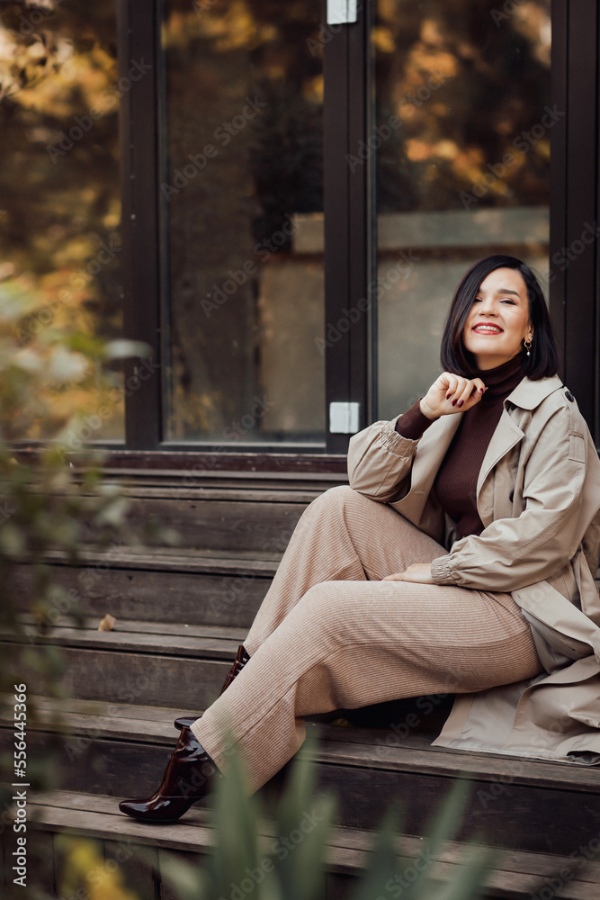 a brunette woman in a raincoat sits on the steps on the streets of autumn city. a brunette woman in a raincoat sits on the steps on the streets of autumn city.