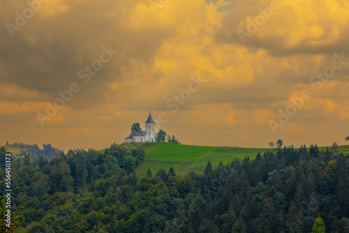 Mountain scenery with church on the mountain ridge. Colorful sunset scenery and cute Saint Primoz church with high mountains in background, Jamnik village, Slovenia, Europe