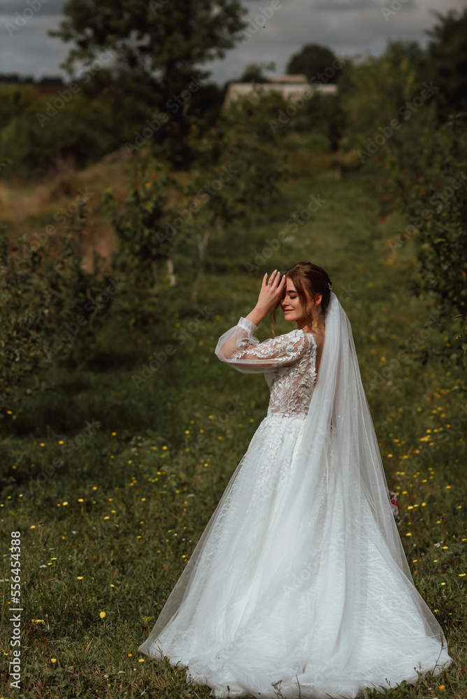 a young beautiful bride poses with a wedding bouquet against the background of nature; the girl is dressed in a white wedding dress; a moment on the wedding day; happy girl expresses her emotions a young beautiful bride poses with a wedding bouquet against the background of nature; the girl is dressed in a white wedding dress; a moment on the wedding day; happy girl expresses her emotions