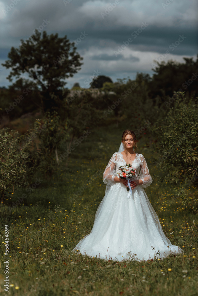 a young beautiful bride poses with a wedding bouquet against the background of nature; the girl is dressed in a white wedding dress; a moment on the wedding day; happy girl expresses her emotions a young beautiful bride poses with a wedding bouquet against the background of nature; the girl is dressed in a white wedding dress; a moment on the wedding day; happy girl expresses her emotions