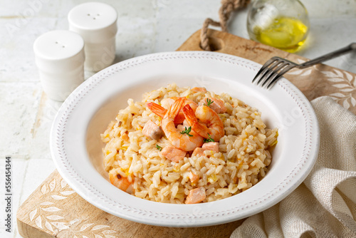 Risotto with prawns, salmon, leek and tangerine. Rice dish. White plate on a light background.