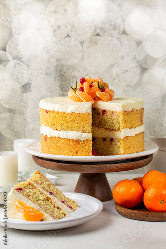 Festive fluffy almond flour sponge cake with cream made of tangerine and orange juice, white chocolate and cream cheese. Decorated with fresh mandarin fryits, cranberries. Homemade. Vertical. photo