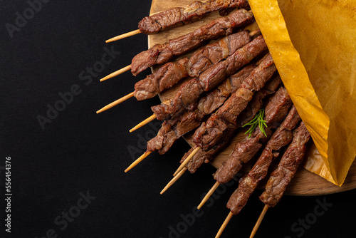 Lamb skewers or kebabs cooked on a brazier, with rosemary and spices. Arrosticini, italian meat dish. Black background, wooden board, copy space.