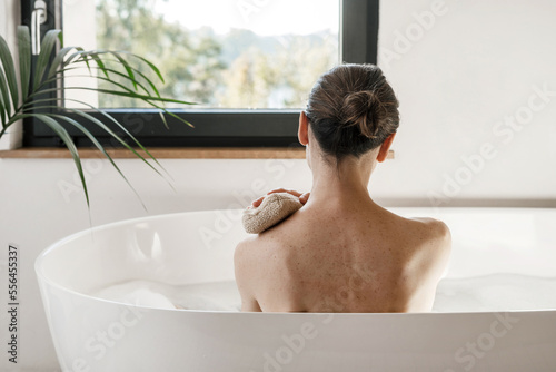 Woman looking at window while she taking a bath, washing body with sponge