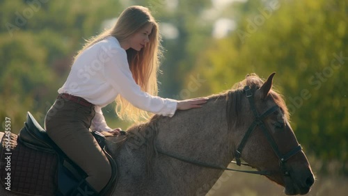 Beautiful girl pets a horse, while sitting on her back. Close up of a horsewoman enjoying beautiful, sunny day in countryside. High quality 4k footage photo
