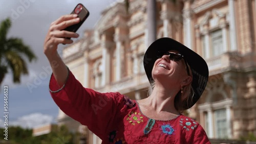 Closeup of pretty, mature elderly woman in ethnic clothing taking selfie with smart phone in front of a mansion, now museum in on the Montejo in Merida, Yucatan, Mexico. photo