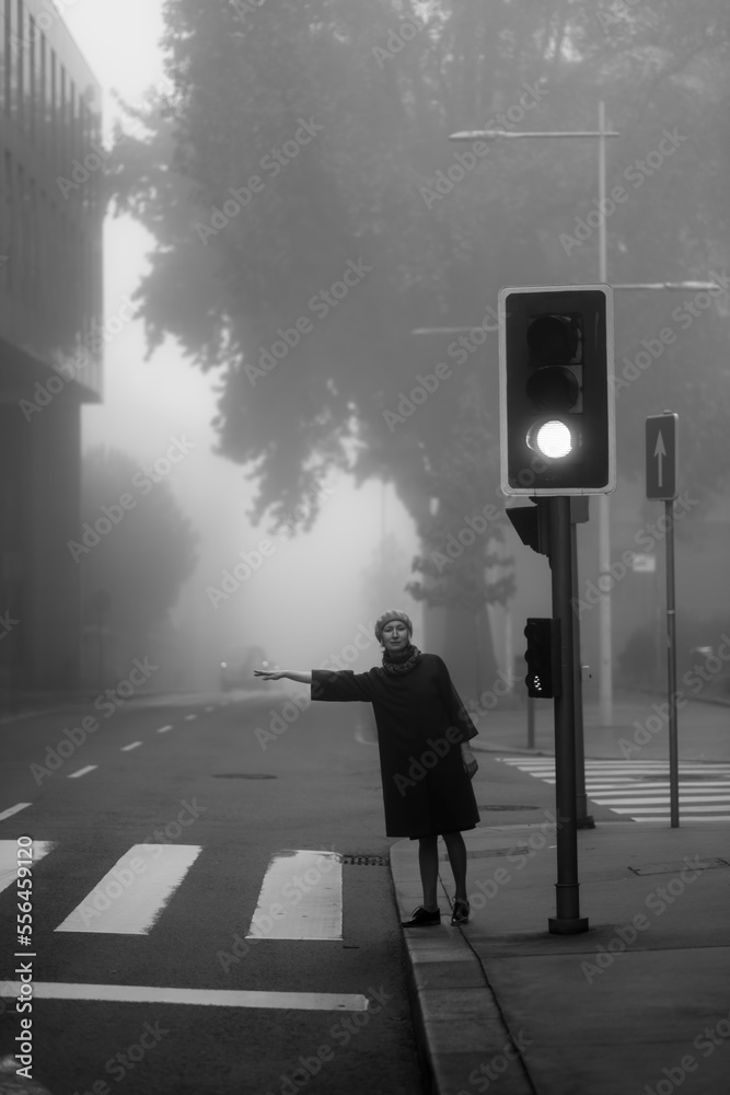 A woman in coat votes in the street in a thick fog. Black and white photo.