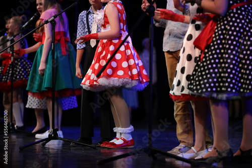 A group of children boys and girls in colorful dresses sing and dance standing on stage at a festive event.The concept of creative leisure and hobbies of young people