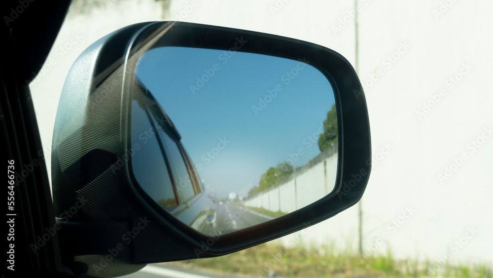 Wing mirror view of car on the road. With reflections of Cement panel over the road bridge. Environment in the day bright.