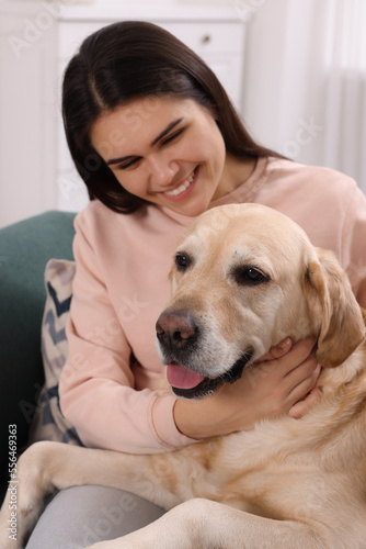 Happy woman with cute Labrador Retriever on sofa at home