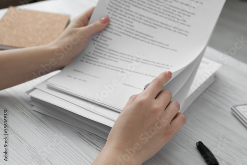 Woman reading documents at white wooden table in office, closeup