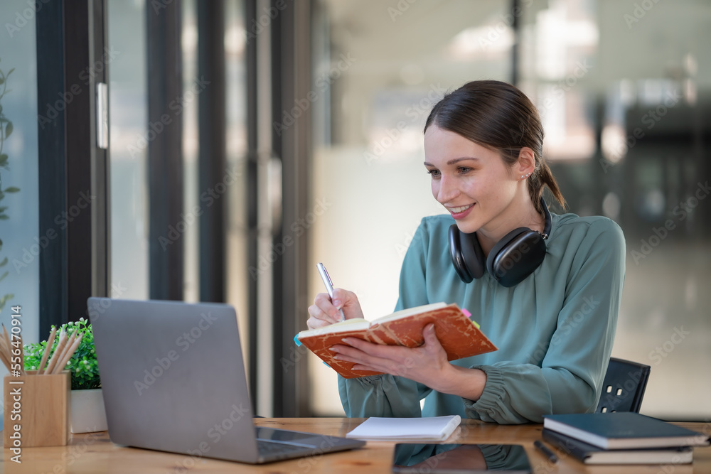 Pretty young businesswoman working on a laptop and taking notes in the office. Pretty young businesswoman working on a laptop and taking notes in the office.